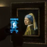 A person taking a picture on an iPhone of a painting of a white woman in a turban.