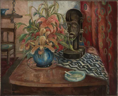 A still life showing a vase with flowers, an African bust sculpture, a cigarette in an ash tray and a table runner, with a curtain behind. 