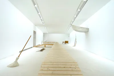 A gallery with a long ramp in it, along with a sculpture resembling a broom and part of a boat coming through a wall.