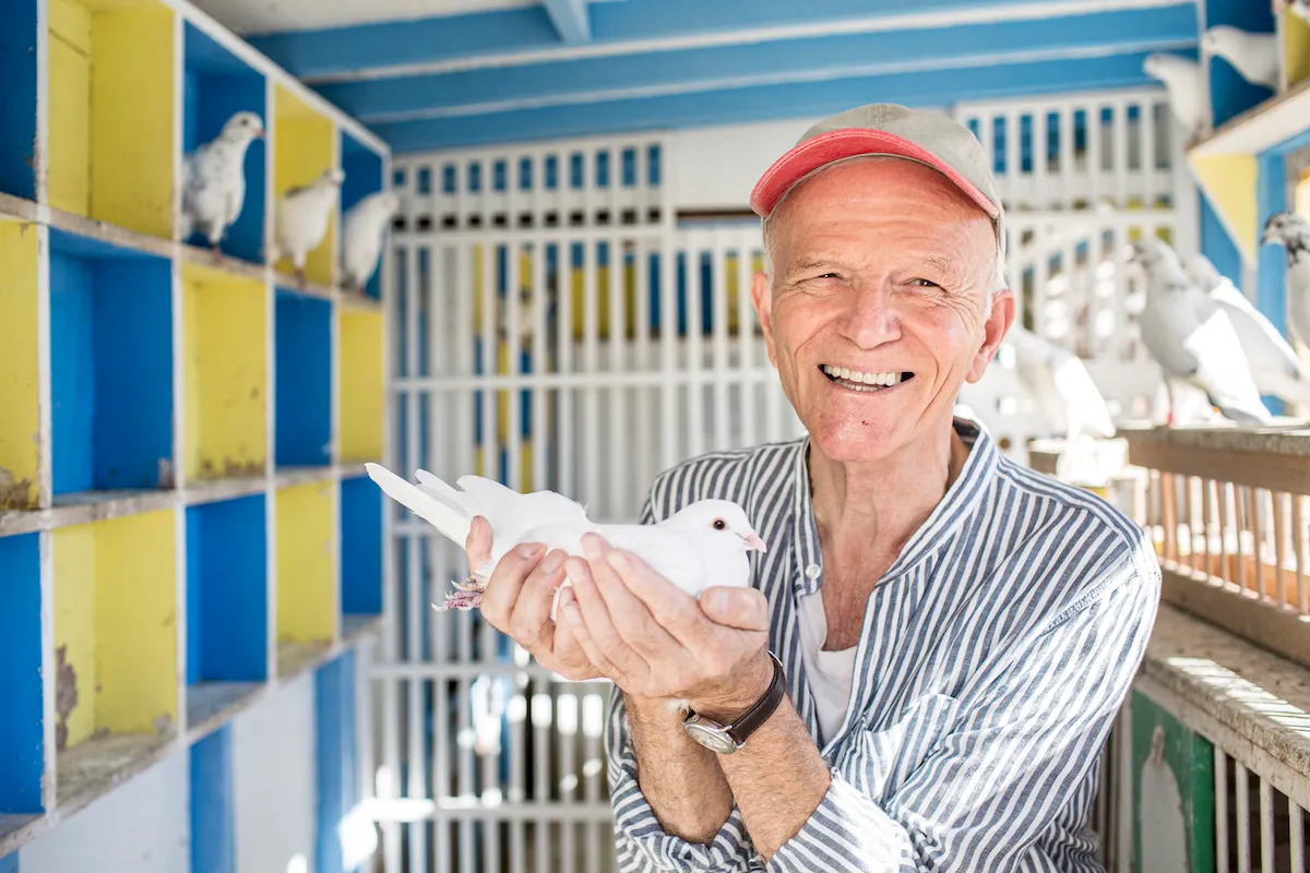 A smiling white man holding a pigeon in his hands.