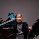 An Asian woman holding the rim of a curved sculpture.