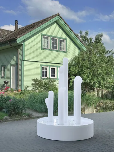 A white sculpture made of cylinders of soap stands in front of a green house. 