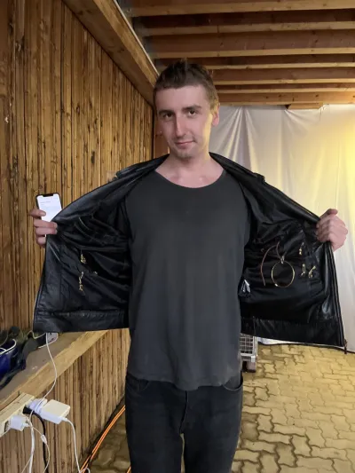 A white man opens a black leather jacket with metal sculptures affixed to the lining. 