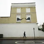 A man passes underneath a new artwork depicting two elephants poking their heads out of blocked out windows unveiled by Banksy on the side of a building at the junction of Edith Grove and Edith Terrace, in Chelsea, south west London. Picture date: Tuesday August 6, 2024. (Photo by Yui Mok/PA Images via Getty Images)