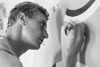 A white man holding a brush to a canvas.