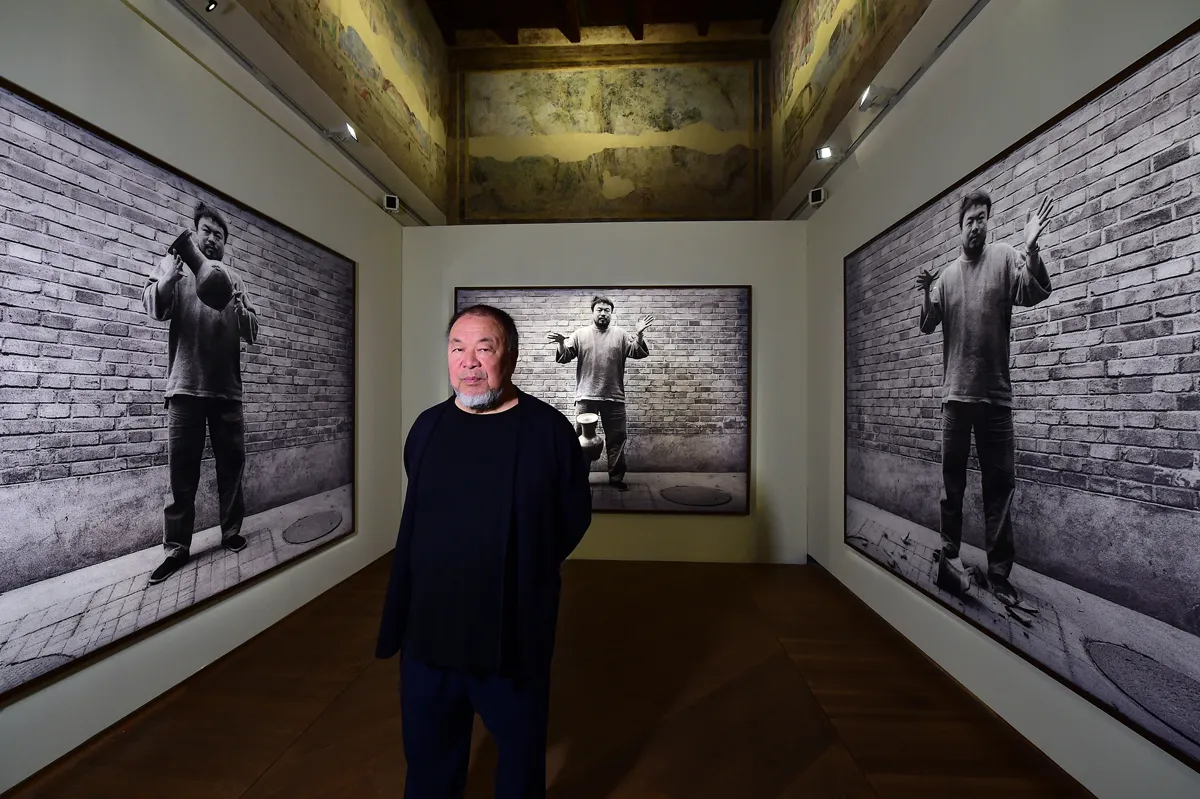 Ai Weiwei stands in front of three of his photographs showing him dropping a Chinese vase.