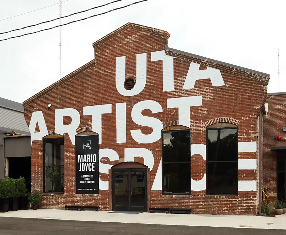 Exterior of a brick-building that had UTA Artist Space painted in white on the facade (though letters are not complete because of the architecture).