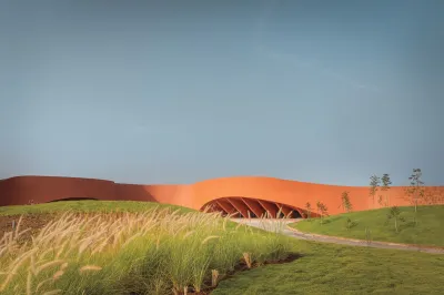 View of an red-orange building that is curving seen from a field in front of it. 