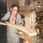 An elderly white woman constructing an arcing wooden sculpture.