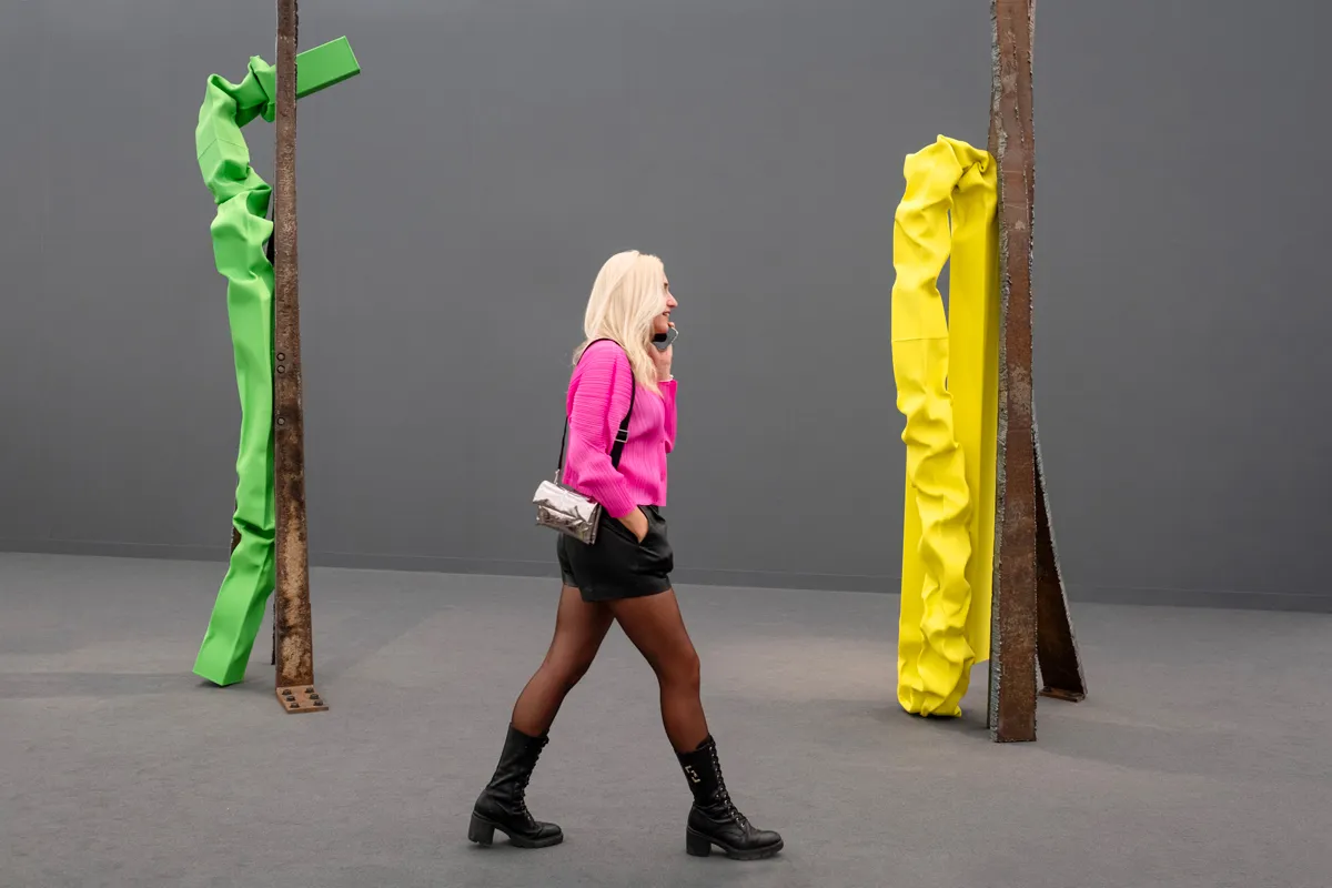 A woman walks by two sets of sculptures made of rusting metal conjoined with a green and a yellow piece of crumpled painted steel.