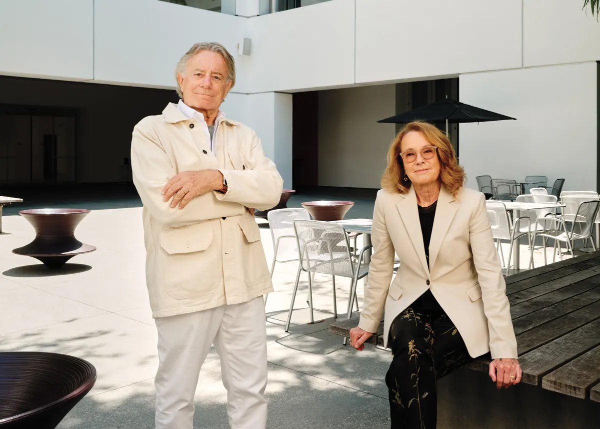 Portrait of Jarl Mohn and Ann Philbin in a courtyard. He is in all white and she has a cream blazer on over all black.