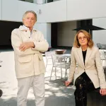 Portrait of Jarl Mohn and Ann Philbin in a courtyard. He is in all white and she has a cream blazer on over all black.