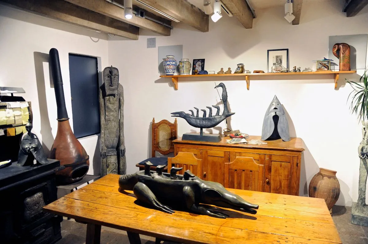 A kitchen with a wood table at its center. On the table is a crocodile-like sculpture of a creature with a long head.