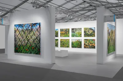 View of an art fair booth showing several paintings of flowers in parks, some are behind chainlink fences.