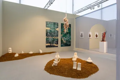 View of an art fair booth showing several white ceramics in brown sand with other works surrounding them.