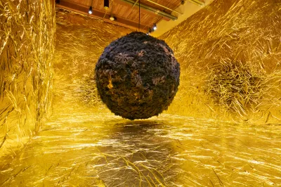 A giant ball formed from synthetic hair in a room lined with golden wallpaper.