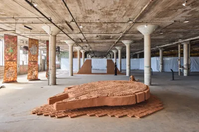 An adobe sculpture atop bricks of adobe in a columned raw space.