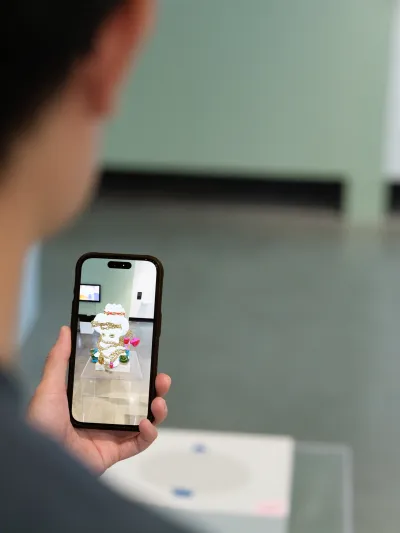 A person holding an iPhone displaying a digital rendering of a sculpture on a pedestal.