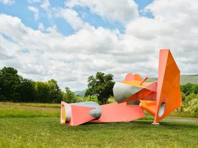 An abstract sculpture composed of pink geometric elements shown on grass.