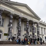 A line of people walking into a museum with banners surroundings its columns.