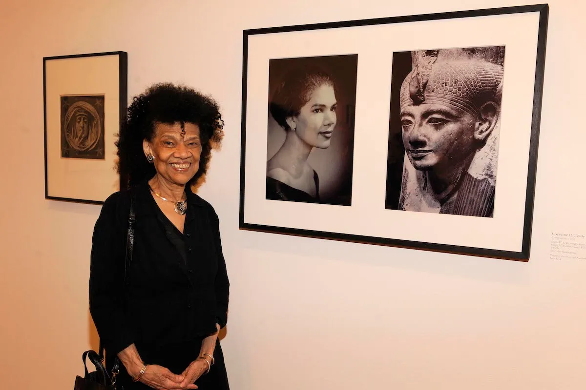 A Black woman standing beside a photograph showing a Black woman beside an ancient Egyptian sculpture.