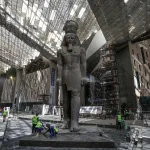 A huge statue of an Egyptian pharaoh with construction workers by its feet.