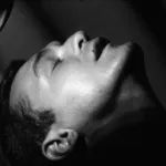 A black-and-white film still of a man with his head back, eyes closed, and mouth slightly ajar, as if relaxed or ecstacy.