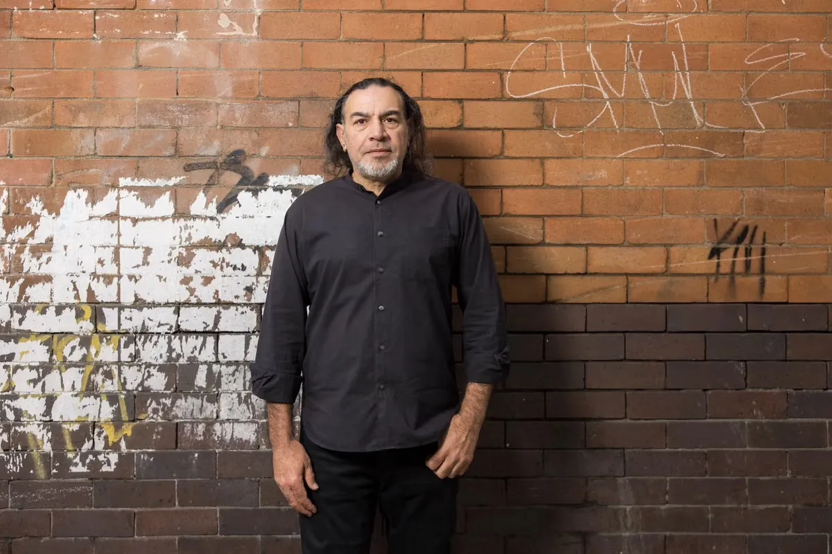 A man pictured against a graffitied brick wall.