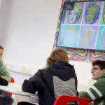 Four students talk beneath a screen showing art.