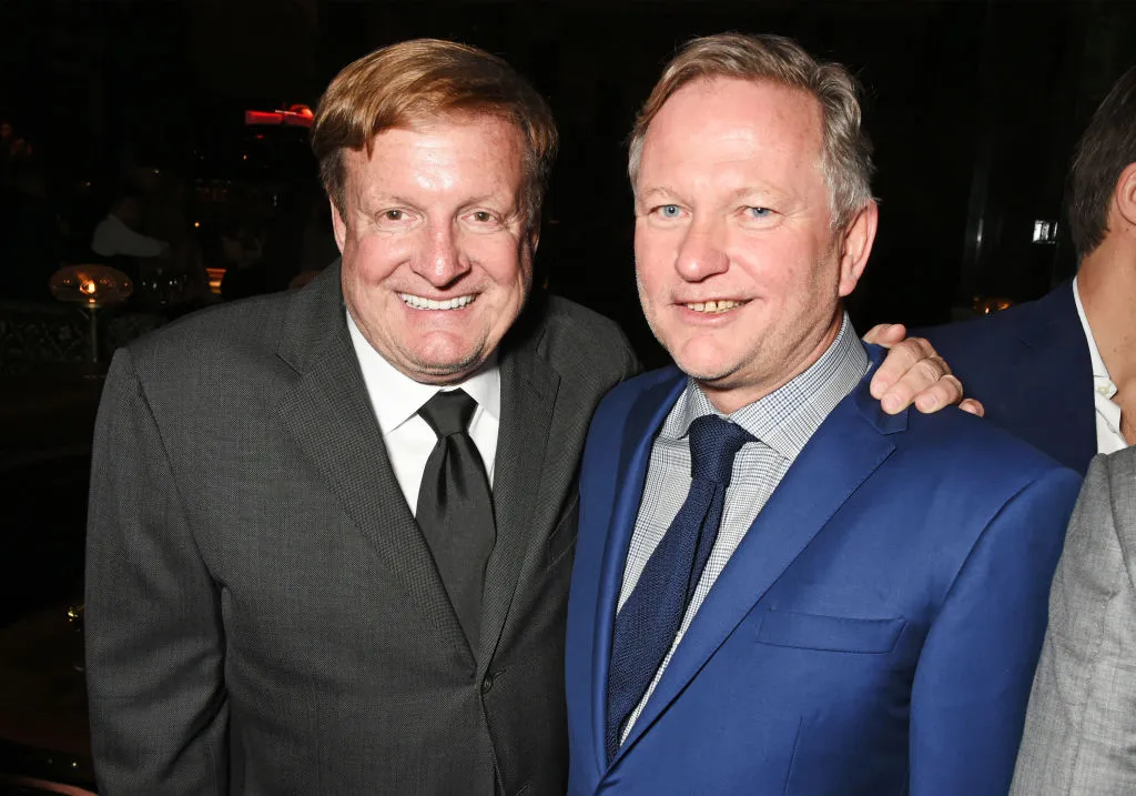 Two men in suits smile for the camera.